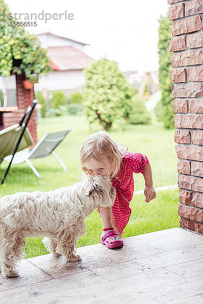 Ein kleines süßes Mädchen im Hof  das einen weißen kleinen Hund küsst