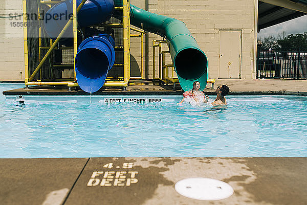 Mann erwischt an sonnigem Tag junges Mädchen am Ende einer Wasserrutsche im Pool
