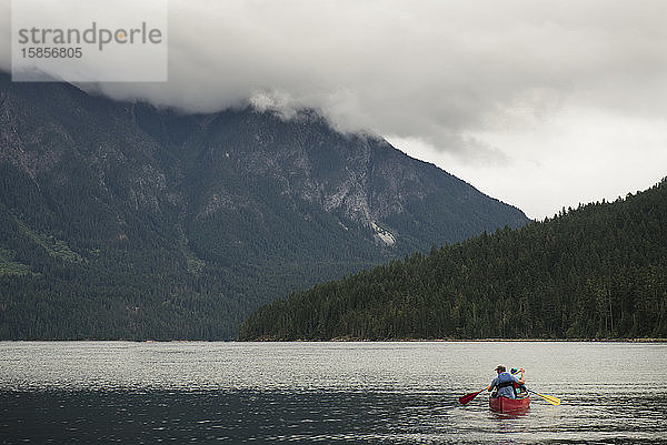 Mann und Kind paddeln mit einem roten Kanu auf einem Bergsee