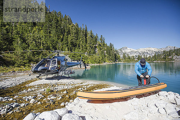 Abenteuerlustiger Mann pumpt aufblasbaren SUP neben einem abgelegenen See auf.