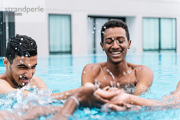 Junger Mann lächelt  während er im Kreis mit einer Gruppe von Freunden in einem Pool spielt