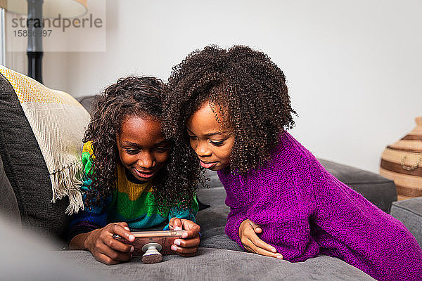 Mädchen schaut Schwester an  die zu Hause auf dem Sofa ein Handy benutzt