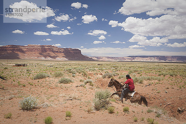 Ein junger Mann reitet auf einem Pferd über eine Ebene in der Nähe des Monument Valley  Arizona