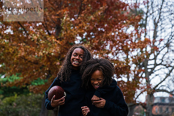 Verspielte Schwestern mit American Football im Herbst im Park