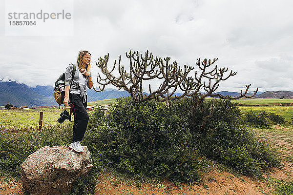 Junge Frau mit einer Kamera steht auf einem Felsen in der Nähe eines Kaktus in Peru