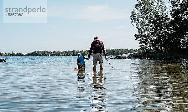 Vater hält die Hand seines Sohnes  während er mit einem Netz im Meer fischt