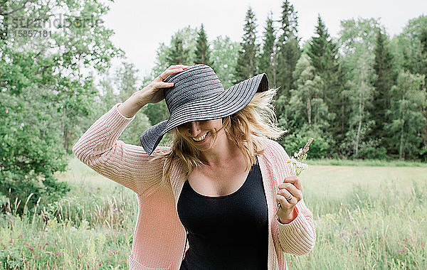 Frau rennt durch ein Feld und hält ihren Hut lächelnd