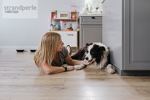 Glückliche Frau lächelt beim Streicheln ihres Hundes zu Hause