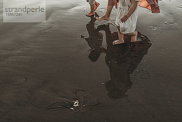 Spiegelung im Meerwasser einer Mutter  die zwei Töchter am Strand spazieren führt
