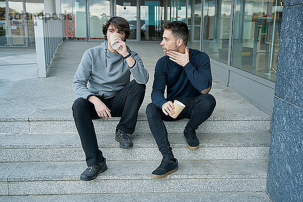 Frontansicht von zwei jungen Männern  die sich unterhalten  auf einer Stadttreppe sitzend und lo