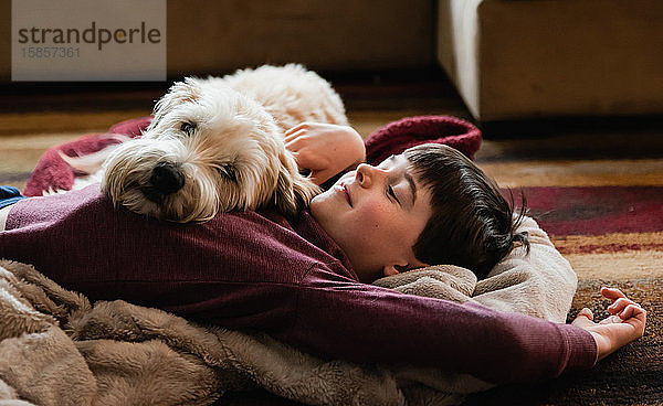 Junge und sein Hund kuscheln sich auf dem Boden auf einer Decke zusammen.