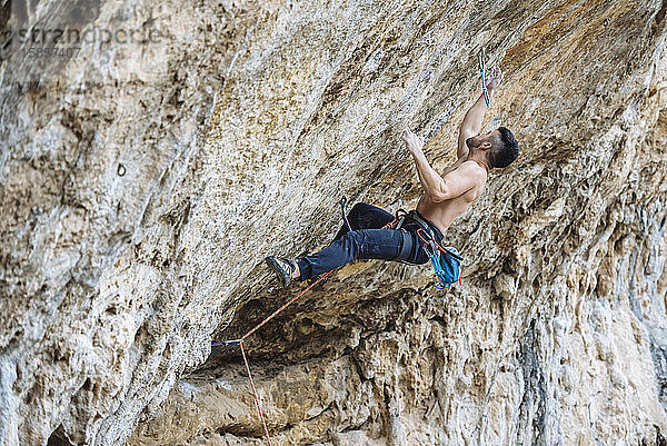 Ein Bergsteiger ohne Hemd schickt eine Sportkletterroute am spanischen Fels.