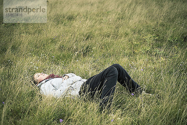 Junge Frau liegt im Gras und träumt vor sich hin.