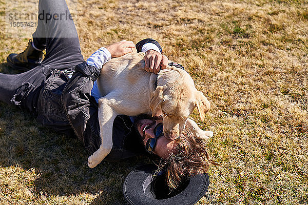 Porträt eines jungen tätowierten Mannes  der mit seinem Hund auf dem Land spielt