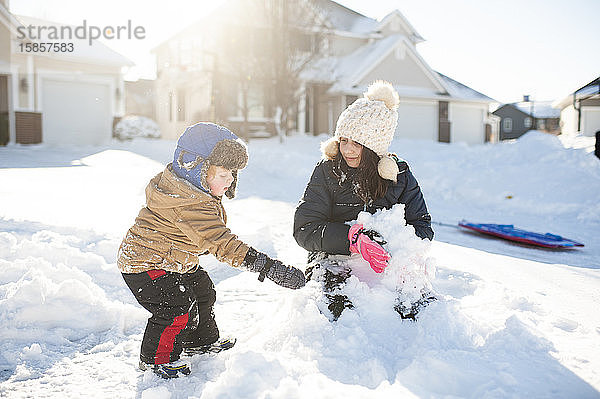 Bruder und Schwester spielen gemeinsam im Schnee vor dem Haus