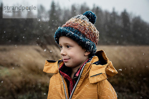 Porträt eines Jungen  der im Schnee steht und im Winter lächelt