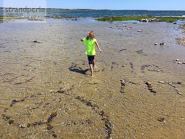 Junge rennt im Sommer mit Felskunst am Strand durch das Gezeitenbecken
