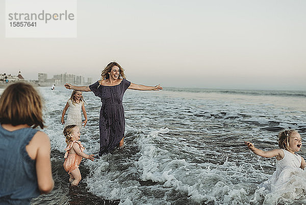 Starke Mutter mit vier Töchtern  die bei Sonnenuntergang im Meer spielen