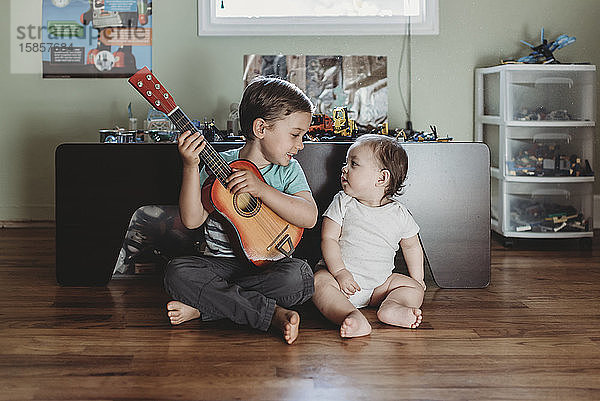 Kleine Schwester und großer Bruder mit Gitarre auf Hartholzboden sitzend