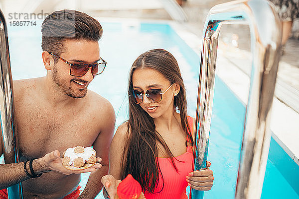 Junges schönes Paar isst Kekse am Pool