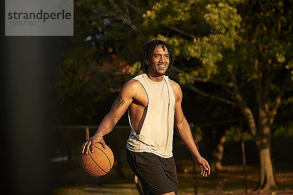 Afroamerikanischer Mann spielt am Nachmittag im Freien Basketball