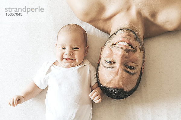 Vater und neugeborener Sohn liegen lachend ausgestreckt im Bett