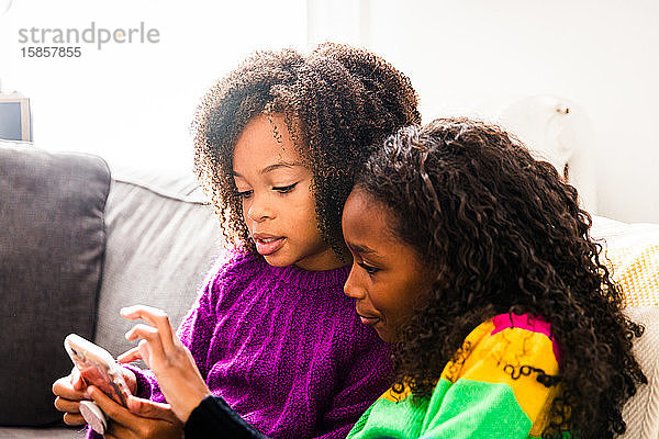 Schwestern in Pullovern  die im Wohnzimmer sitzen und auf ihr Handy schauen