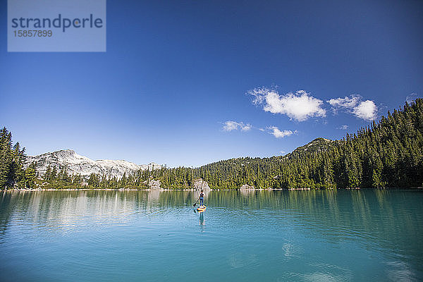 Fitte Frau paddelt stehendes Paddelbrett auf blauem See.