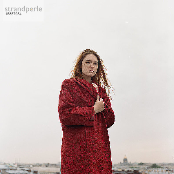 Bildnis einer schönen brünetten Frau in rotem Mantel auf dem Dach stehend
