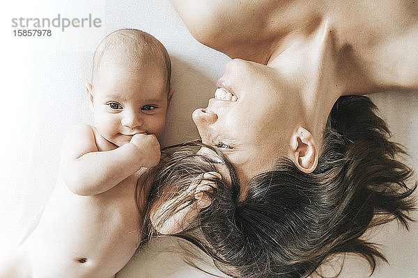 Mutter und neugeborener Sohn liegen ausgestreckt im Bett  der Sohn fängt die Haare der Mutter  und sie schaut ihn mit Liebe an