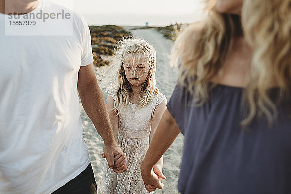 Ernsthaftes Mädchen mit traurigem Gesicht beim Spaziergang mit den Eltern am Strand