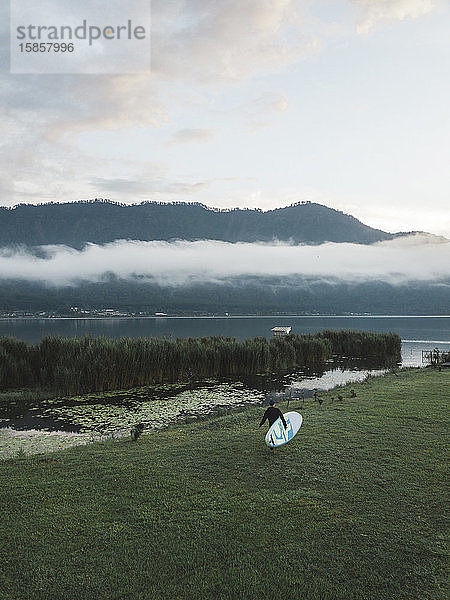 Junger Mann mit Surfbrett in der Nähe des Bratan-Sees