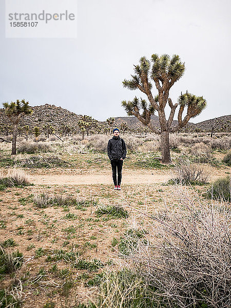 Junger Mann neben großem Joshua-Baum in der Wüste am Weg