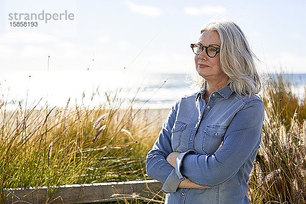 Nachdenkliche Frau mit verschränkten Armen steht am Strand von Manhattan am sonnigen Tag am Himmel