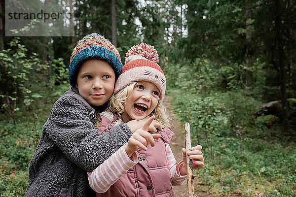 Bruder umarmt lachend seine Schwester beim Spaziergang durch den Wald