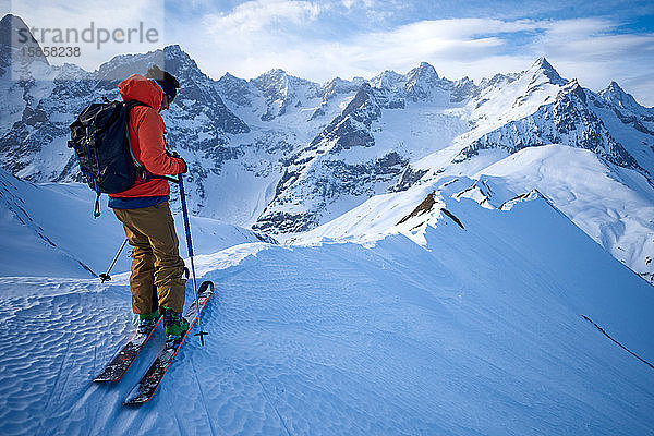 Skifahrer in orangefarbener Jacke auf Bergrücken