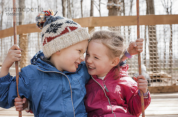 Mädchen und Junge auf einer Schaukel  die zusammen draußen spielen und lachen
