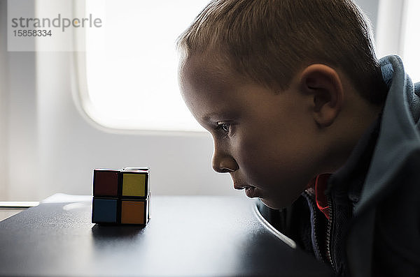 Porträt eines Jungen  der sich im Flugzeug ein Rubix-Würfel-Spiel ansieht