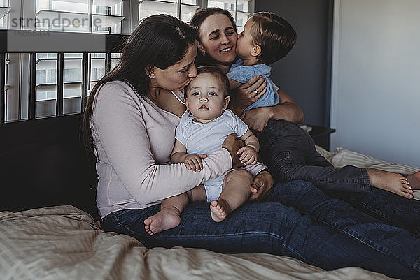 Glückliche Familie mit zwei Müttern  die zu Hause im Schlafzimmer kuscheln