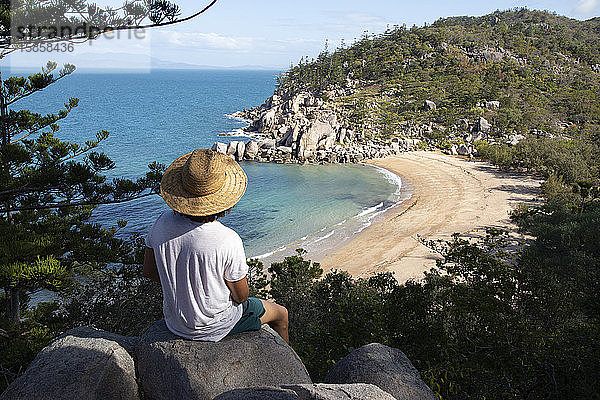 Lockenkopf mit Hut und Badeanzug auf einem Felsen  der die Bucht bewundert