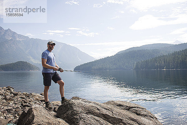 Mann steht auf Felsen und angelt am Ross Lake im Bundesstaat Washington