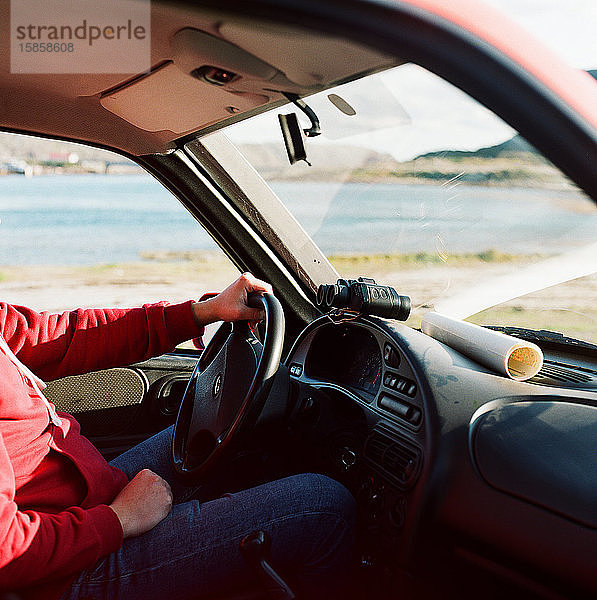 Ein Mann sitzt am Steuer eines Autos mit einer Karte und einem Fernglas