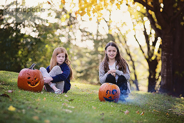 Zwei junge Mädchen sitzen im Herbst draußen und rauchen Kürbisse