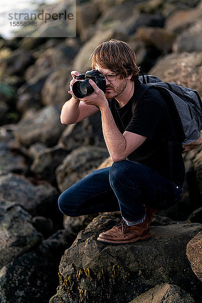 Junger Mann beim Fotografieren in der Hocke auf Stein