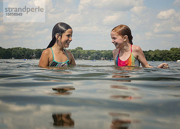 Zwei junge Mädchen in Badeanzügen spielen im Wasser in einem See