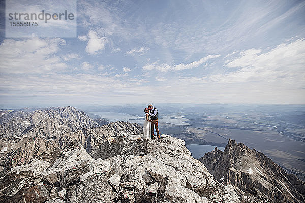 Frisch vermähltes Paar küsst sich auf dem Gipfel eines wunderschönen  felsigen Berges