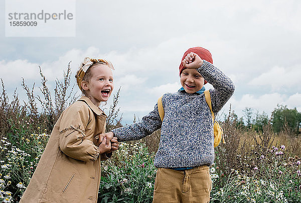 Bruder und Schwester halten sich lachend an den Händen und spielen draußen