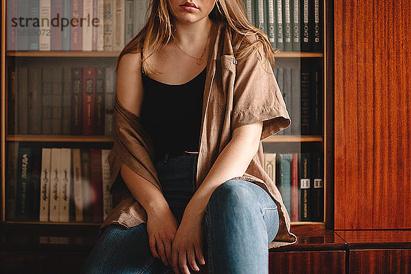Ausgeschnittenes Bild eines Teenagers  der am Bücherregal sitzt
