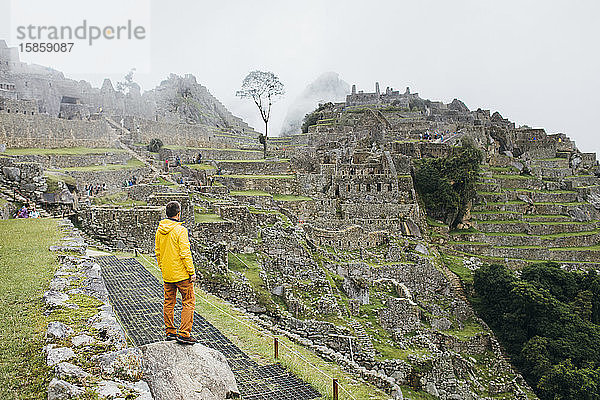 Ein Mann in gelber Jacke steht in der Nähe der Ruinen von Machu Picchu  Peru