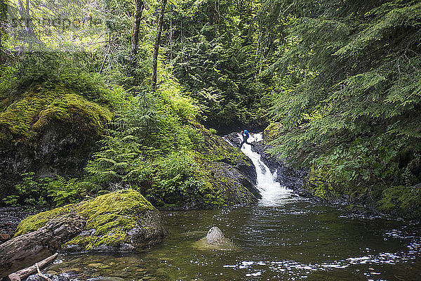 Backpacker springt in einer abgelegenen Gegend über einen Wasserfall.